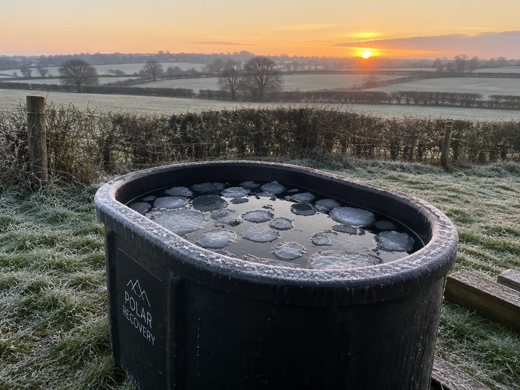 A realistic plastic cold plunge tub with floating ice in a frosty Suffolk field at sunrise